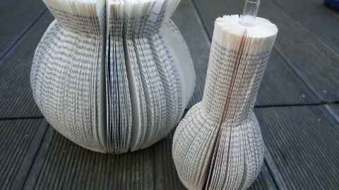 Zwei dekorative Buchvasen aus gefalteten Buchseiten stehen auf einem Holztisch, kreativ gestaltet für ein DIY-Projekt.