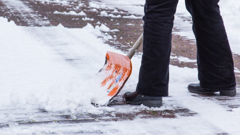 Jemand schaufelt Schnee auf einem Gehweg, trägt rutschfeste Schuhe und arbeitet bei Schneematsch und Glätte.