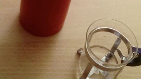 Ein transparentes Glas mit warmem Wasser steht auf einem Tisch neben einem roten Becher, der Kältegefühl lindern soll.