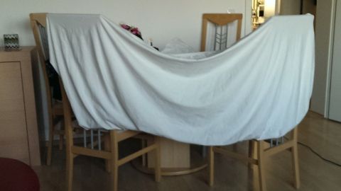Ein Spannbettlaken wird über Stühle gelegt, um es nach dem Waschen zum Trocknen auszustrecken. Der Raum wirkt hell und wohnlich.