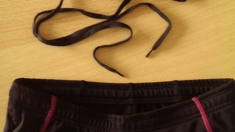Einen alten Schnürsenkel einziehen und es kann wieder losgehen Eine Hose mit losem Zugband liegt auf einem Tisch, während Schnürsenkel daneben liegen, bereit zum Ersetzen.