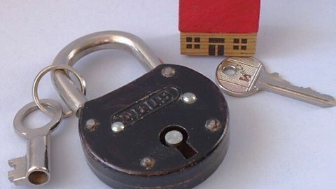 Ein großer Vorhängeschloss liegt neben einem kleinen Haus und einem Schlüssel, der Sicherheit und den Schlüssel verstecken symbolisiert.