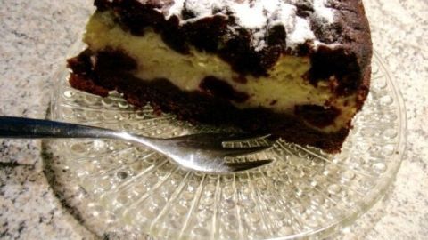 Eine saftige Schoko-Kirsch-Käsetorte liegt auf einem Glasteller, während eine Gabel neben ihr bereitliegt.