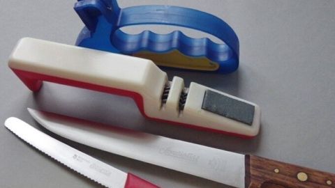 Ein Messerschärfer liegt neben einem Küchenmesser auf einer grauen Oberfläche, bereit, um die Klinge zu schärfen.