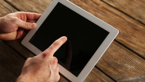 Ein Tablet wird mit einem Finger gereinigt, während es auf einem Holztablett liegt, um Schmutz zu entfernen.