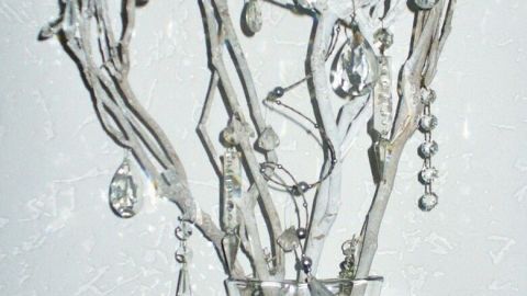 Äste mit glitzernden Anhängern stehen in einer klaren Vase, umgeben von dekorativem glitzerndem Material und Gläsern.