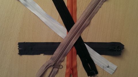 Sechs Reißverschlüsse in verschiedenen Farben liegen kreuz und quer auf einem hellen Untergrund.