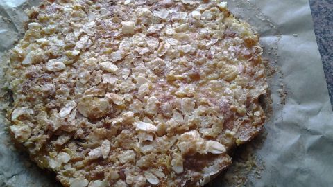 Ein Apfelkuchen liegt auf Backpapier, leicht braun mit Haferflocken und einer knusprigen Oberfläche in einer modernen Küche.