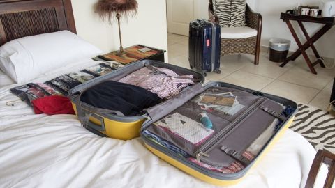 Ein geöffneter Reisekoffer liegt auf einem Bett, während Kleidung und Zubehör zum Packen bereitliegen.