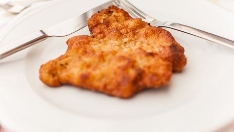 Ein paniertes Schnitzel liegt auf einem weißen Teller und wartet darauf, serviert zu werden, um genossen zu werden.