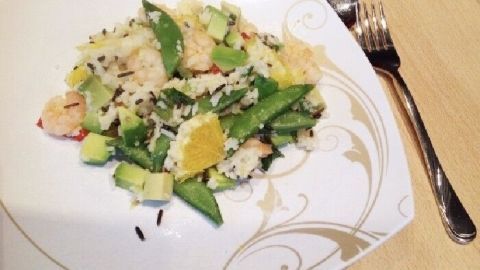 Ein buntes Gericht aus Avocado-Reis mit Garnelen liegt auf einem weißen Teller. Es wird von einer Gabel begleitet.
