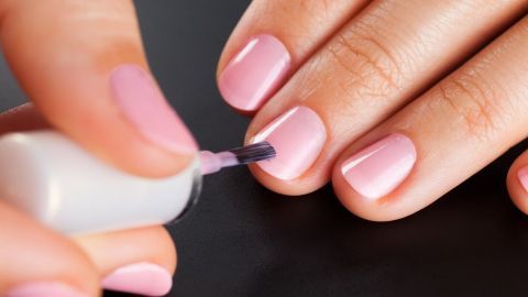 Eine Hand trägt pinken Nagellack auf die Fingernägel, die auf einem dunklen Untergrund liegen.