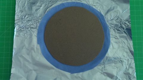 Ein runder Stoffkreis liegt auf Aluminiumfolie, während er auf einer grünen Unterlage für ein kreatives Projekt vorbereitet wird.