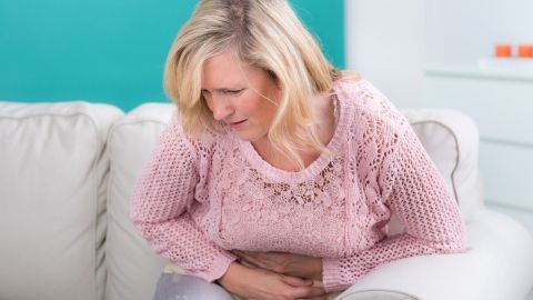 Eine Frau sitzt auf einem Sofa und hält sich den Bauch, offensichtlich unwohl, was auf Verstopfung hinweisen könnte.