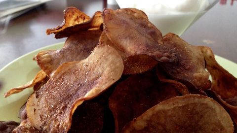 Knusprige Kartoffelchips liegen auf einem Teller, während ein Glas mit Dip daneben steht, ideal zum Snacken.