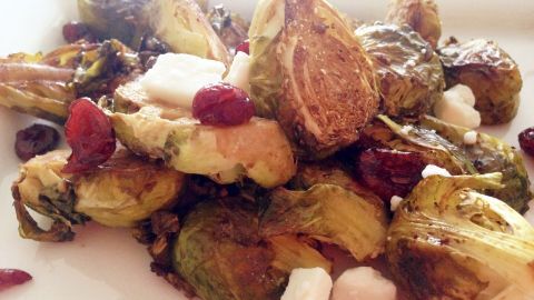 Gerösteter Rosenkohl wird zusammen mit Cranberrys und Ziegenkäse in einer weißen Schüssel angerichtet.