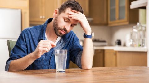 Ein Mann sitzt am Tisch mit einem Glas Wasser und hält seine Stirn, während er Sodbrennen zu empfinden scheint.