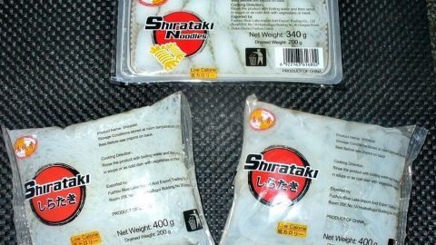 Shirataki-Nudeln aus Konjakwurzel liegen verpackt auf einer dunklen Oberfläche, bereit zur Verwendung in der Küche.