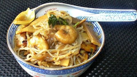 Eine Schüssel Konjaknudeln mit Knoblauchgarnelen, garniert mit Kräutern, auf einem schwarzen Untergrund.