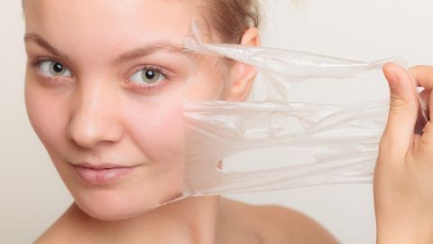 Eine junge Frau zieht vorsichtig eine transparente Peel-Off Maske von ihrem Gesicht in einer hellen Umgebung ab.