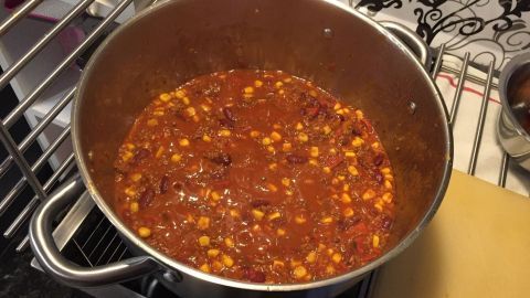 Ein großer Topf mit würzigem Chili köchelt auf einem Herd in einer modernen Küche, umgeben von Kochutensilien.