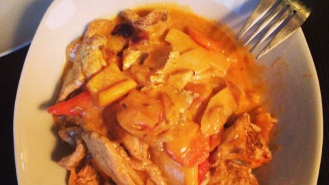 Ein schmackhaftes Thai-Curry liegt in einer weißen Schüssel, umgeben von einem dunklen Tisch und Besteck.