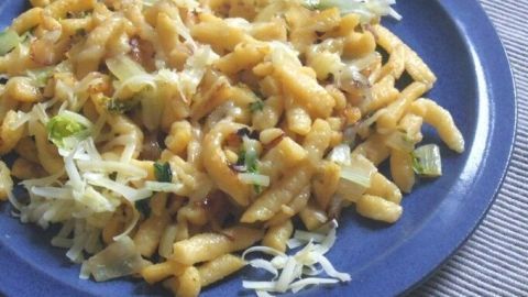 Eine Portion Spätzle liegt auf einem blauen Teller, während frischer, gebratener Salat darüber verstreut ist.