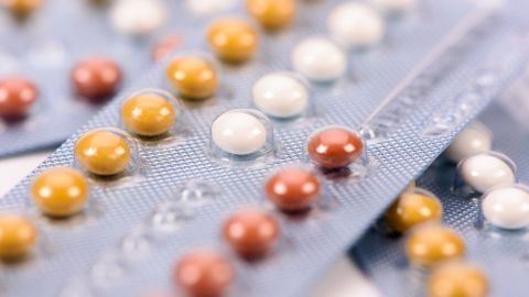 Bunte Pillen liegen auf einer blauen Blisterverpackung, die verschiedene Verhütungsoptionen zeigt, ohne die Pille hervorzuheben.