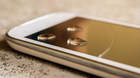 Ein Smartphone liegt mit Wassertropfen auf der Oberfläche, es funktioniert wieder nach dem Mitwaschen in der Waschmaschine.