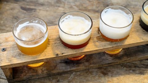 Vier Gläser Bier stehen auf einem Holzbrett, präsentieren verschiedene Farben und Schaum, perfekt für eine Verkostung.