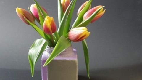 Eine kleine Vase aus Gips hält bunte Tulpen, während sie vor einem schwarzen Hintergrund steht und frischen Farbtupfer bringt.