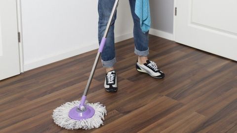 Eine Frau putzt den glatten Boden mit einem Wischmopp in einem hellen Raum, um ihn sauber und ordentlich zu halten.