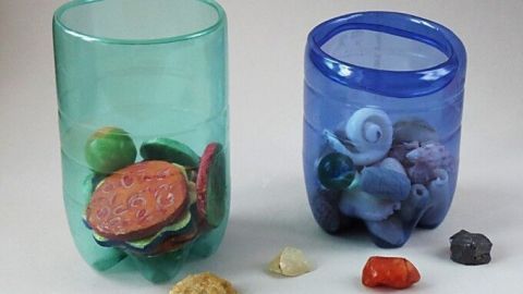 Zwei Behälter aus Mineralflaschen sind mit bunten Steinen gefüllt und stehen auf einer neutralen Oberfläche.