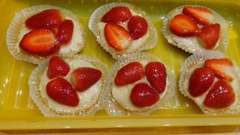 Sechs Kokos Cupcakes liegen in einer gelben Schale, garniert mit frischen Erdbeeren auf cremigem Topping.
