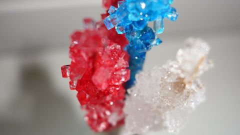 Bunte Kandiszucker-Sticks stehen in einem Glas und leuchten im Licht, während sie auf einer weißen Fläche präsentiert werden.