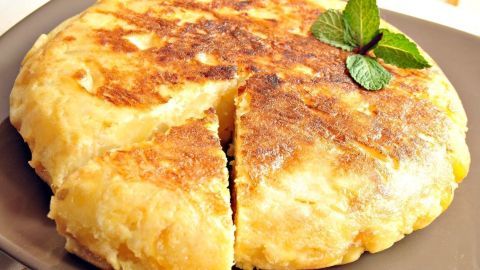 Eine goldbraune spanische Tortilla de Patatas liegt auf einem Teller, mit frischen Kräutern garniert und teilweise geschnitten.