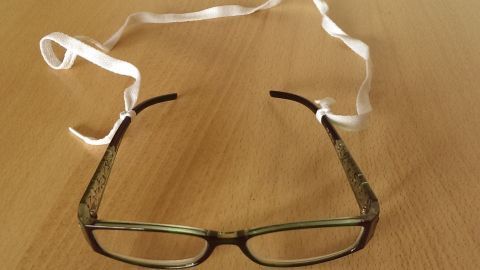 Eine Brille liegt auf einem Holztablett, während Schnürsenkel um die Bügel geschlungen sind, um sie zu sichern.