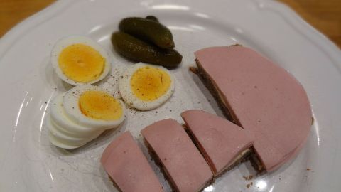 Auf einem weißen Teller liegen hartgekochte Eier, geschnittene Wurst und Gewürzgurken, bereit zum Servieren.