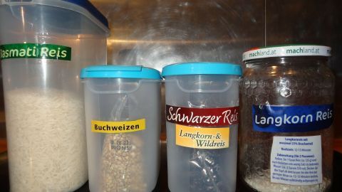Vorratsdosen sind kreativ beschriftet und stehen in einer Reihe auf der Küchentheke, gefüllt mit verschiedenen Reissorten.