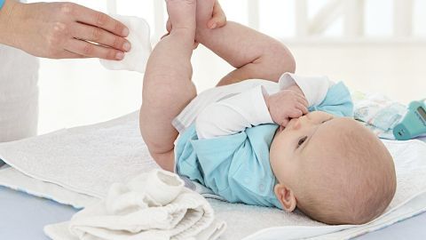 Ein Baby liegt auf einer Wickelunterlage, während eine Person den wundem Babypo mit einem Feuchttuch reinigt.