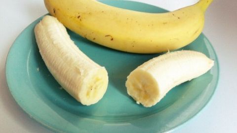 Eine ganze Banane und zwei halbierte Bananen liegen auf einem türkisfarbenen Teller und zeigen die gesunde Pracht der Bananen.