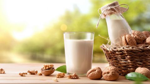 Ein Glas Walnussmilch steht auf einem Holztisch, umgeben von zerbrochenen Walnüssen und frischen Blättern.