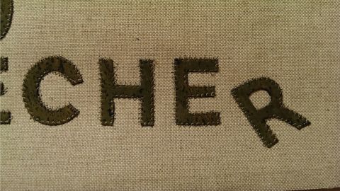 Ein helles Gewebe zeigt in großen, kräftigen Buchstaben das Wort "RECHER". Es wirkt fest und strukturiert, um Nähkünste darzustellen.