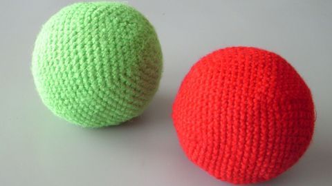 Zwei gestrickte Bälle in Grün und Rot liegen nebeneinander auf einer Fläche, ideal als haltbares Hundespielzeug zum Spielen.