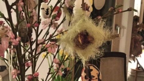 Wollgarnkreuze hängen dekorativ an einem blühenden Zweig, um einen festlichen Osterstrauß im gemütlichen Raum zu gestalten.