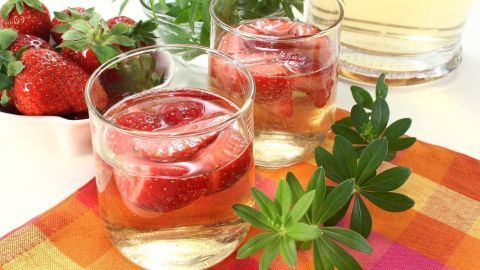 Gläser mit Maibowle und frischen Erdbeeren stehen auf einem bunten Tisch, umgeben von weiteren Erdbeeren und Kräutern.
