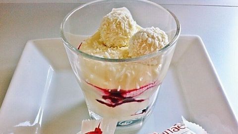 Eine Schüssel mit Raffaellocreme und Beeren ist auf einem Teller platziert, umgeben von zwei unversehrten Raffaello-Verpackungen.