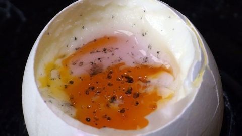 Ein Frühstücksei mit schwarzem Salz, das in einer aufgeschlagenen Eierschale liegt, auf dunklem Hintergrund sichtbar.