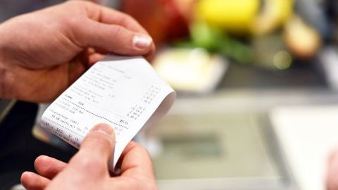Eine Person hält einen Kassenzettel in der Hand, während im Hintergrund frisches Obst sichtbar ist, was auf Umtauschmöglichkeiten hinweist.