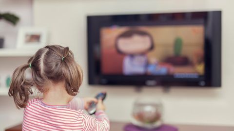 Ein Kind mit Zöpfen sitzt vor einem Fernseher und schaut eine Zeichentrickserie über einen grünen Kaktus.